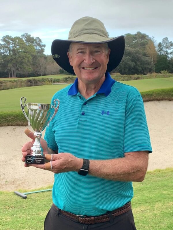A man holding a trophy in front of some sand dunes.