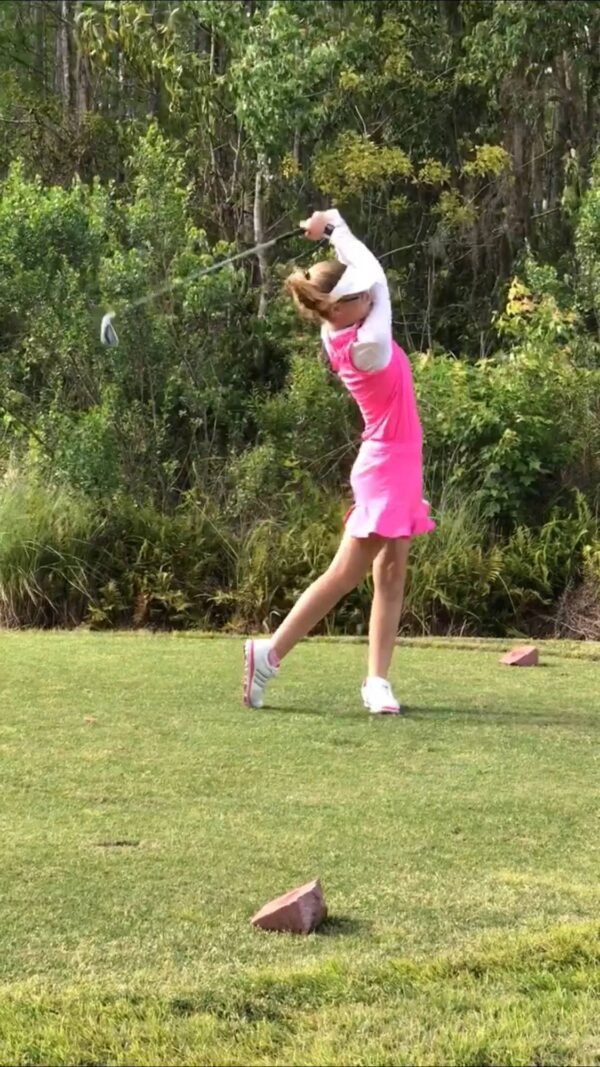 A woman in pink is swinging at the golf ball.