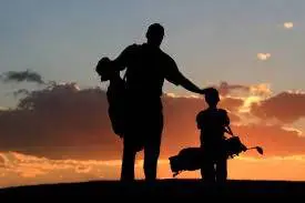 A man and child holding hands in front of the sunset.