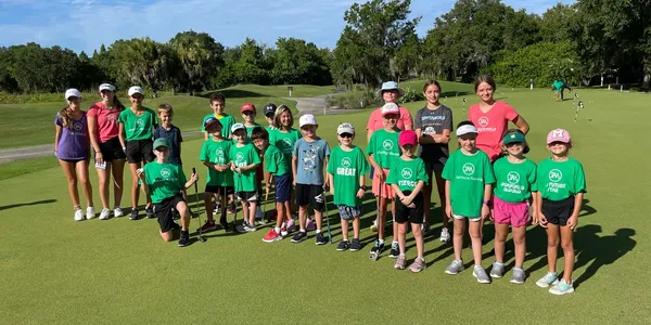 A group of children standing on top of a golf course.